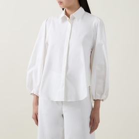 Model wearing Akris Punto cream shirt with voluminous balloon sleeves and button front, styled with white wide-leg trousers.