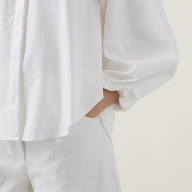 Model wearing Akris Punto cream shirt with relaxed silhouette and cuffed sleeves, styled with matching cream trousers