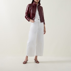 Model wearing Akris Punto cream shirt, styled with burgundy patent zip-up jacket, white wide-leg cropped trousers and brown strappy heels.