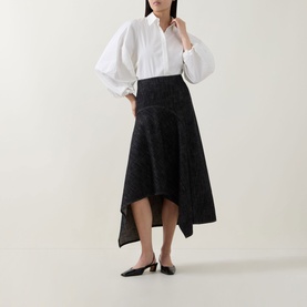 Model wearing Akris Punto Black Denim skirt with asymmetric hem, styled with white balloon-sleeve blouse and black kitten heels.