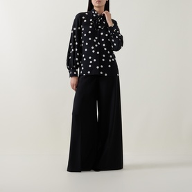 Model wearing Akris Punto black-cream star print shirt with wide-leg black trousers, full-length view.