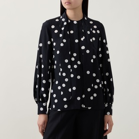Model wearing Akris Punto black-cream polka dot blouse with tie neck, balloon sleeves and cuffed wrists, paired with black trousers.