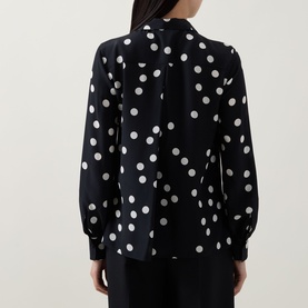 Model wearing Akris Punto black and cream polka dot shirt, rear view, long sleeves with buttoned cuffs, relaxed fit.