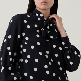 Model wearing Akris Punto black-cream polka dot shirt with puff sleeves and front tie neck detail, styled close-up view.