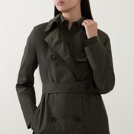 Model wearing Akris Punto olive double-breasted trench coat with belt and collar detail, hands in pockets