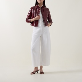Model wearing Akris Punto cream wide-leg trousers, styled with a burgundy patent jacket and strappy heeled sandals.