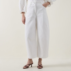 Model wearing Akris Punto cream wide-leg trousers with front pleat detail, styled with a white blouse and dark heeled mules.