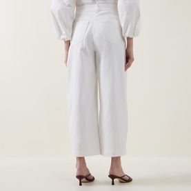 Model wearing Akris Punto cream wide-leg trousers, back view, styled with a white puff-sleeve top and brown heeled mules.