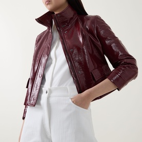 Model wearing Akris Punto cream trousers styled with a burgundy patent cropped jacket with zip front and funnel neck.