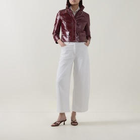 Model wearing Akris Punto cream wide-leg trousers, styled with a burgundy patent cropped jacket and brown heeled mules.