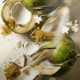 Byredo Body Mist lifestyle shot featuring fresh coconuts, white flowers, and golden brown sugar crystals on a light surface