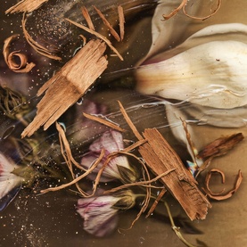 Byredo Body Mist fragrance notes flatlay featuring dried flowers, cinnamon bark, and botanical ingredients with golden glitter accents