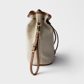 Prada Accessories neutral canvas bucket bag with tan leather trim, drawstring top, and gold-tone hardware with detachable wrist strap.