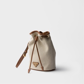 Prada Accessories neutral canvas bucket bag with tan leather trim, drawstring top, gold triangle logo, and adjustable shoulder strap