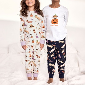 Two children wearing Chelsea Peers Halloween Dogs Multi pyjama sets featuring dachshund dog and pumpkin prints in cream and navy