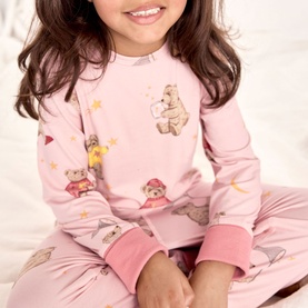 Model wearing pink long-sleeve pyjama set with illustrated bear and star print, pink ribbed cuffs, children's fit