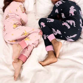 Two children lying on white bedding wearing pink and navy printed pyjama sets with contrast cuffs