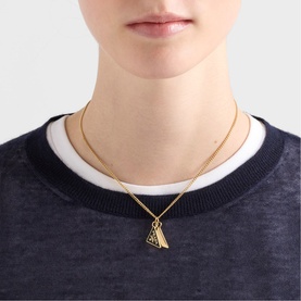 Model with Prada Accessories gold and silver tone pendant necklace on fine chain, worn over navy blue sweatshirt.