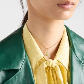 Model with gold chain necklace featuring a triangular green stone pendant, styled with a green leather jacket and yellow polka dot scarf