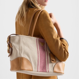 Model carrying Prada Accessories neutral canvas and tan leather tote bag with pink stripe detail and gold hardware, worn over shoulder