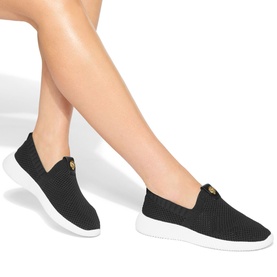 Model wearing Kurt Geiger London black knit slip-on trainers with gold-tone emblem detail and white chunky sole.