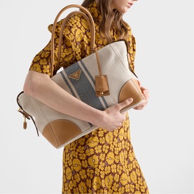 Model carrying Prada Accessories neutral canvas and tan leather tote bag with gold hardware, styled with a yellow floral dress.
