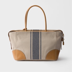 Prada Accessories neutral canvas tote bag with navy stripe detail, tan leather handles, corner trim, and gold-tone zip fastening