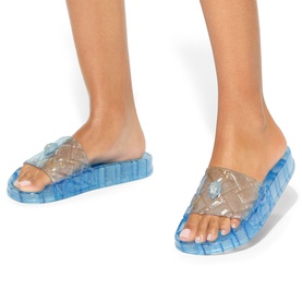 Model wearing Kurt Geiger London blue transparent clear strap slides with quilted blue rubber sole, shown from ankles down.