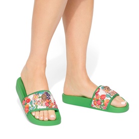 Model wearing Kurt Geiger London white floral print slides with green sole and footbed, feature multicolour tropical print strap.