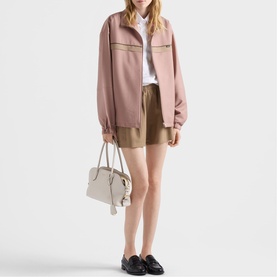 Model carrying a grey structured top-handle bag with chain strap, styled with pink zip-up jacket, white shirt, khaki shorts and black loafers.