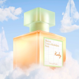 Maison Francis Kurkdjian Kurky Eau de Parfum in peach-toned square bottle with sage green cap, set against a pastel blue cloudy sky