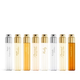 Maison Francis Kurkdjian fragrance set of 7 miniature travel spray vials with gold and silver caps, varying from clear to amber tones.