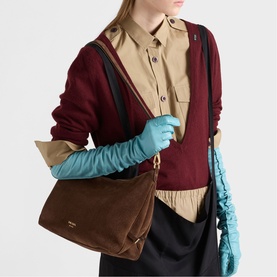 Model carrying Prada Accessories brown suede shoulder bag with gold hardware, styled with burgundy knit and teal gloves