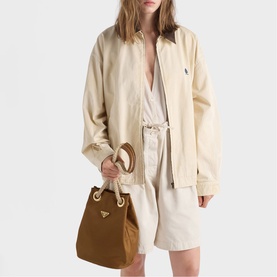 Model carrying Prada Accessories brown bucket bag with gold hardware and rope handles, styled with cream jacket and shorts set.