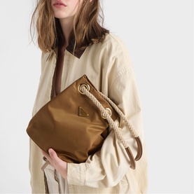 Model carrying Prada Accessories brown nylon pouch bag with gold rope detailing, styled with a beige oversized jacket.