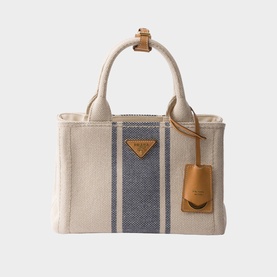 Prada Accessories neutral canvas tote bag with navy stripe detail, tan leather top handles, gold-tone triangle logo plaque and luggage tag.