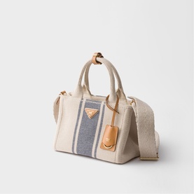Prada Accessories neutral canvas tote bag with navy stripe detail, gold-tone triangle logo, tan leather tag and woven shoulder strap.