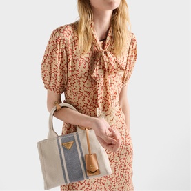 Model carrying Prada Accessories neutral canvas tote bag with gold-tone triangle logo, styled with a floral midi dress