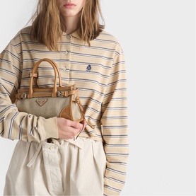 Model carrying Prada Accessories neutral canvas mini tote bag with tan leather handles and gold-tone hardware, styled with a striped shirt