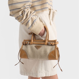 Model carrying Prada Accessories neutral canvas small tote bag with tan leather trim, gold-tone hardware, and twin top handles, styled with cream