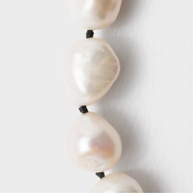 Close-up of white baroque freshwater pearl necklace with black knotted silk cord between each pearl