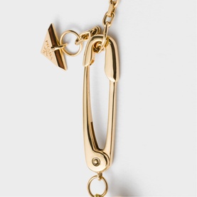 Gold-tone chain necklace with oversized safety pin pendant and logo charm detail, on white background