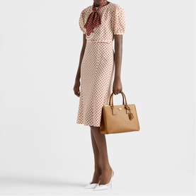 Model carrying Prada Accessories brown structured tote bag with gold-tone hardware, styled with polka dot dress and white heels
