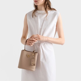 Model carrying Prada Accessories powder small structured bucket bag with gold-tone hardware and short top handles, styled with white sleeveless dress