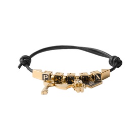Prada black leather bracelet with gold-tone letter cube charms, key and skull pendants on knotted cord