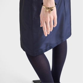 Model with gold charm bracelet styled with navy mini dress and ribbed tights