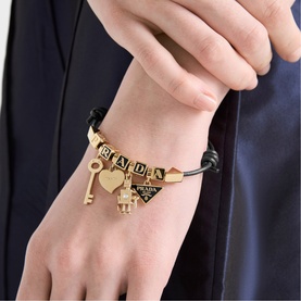 Model with black leather bracelet featuring gold-tone Prada triangle logo charm, key, heart and letter charms on wrist