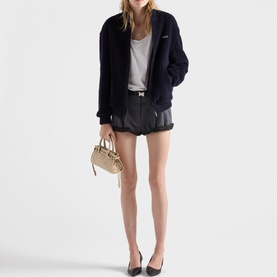 Model carrying Prada Accessories neutral handbag, styled with navy zip-up jacket, grey vest, black leather shorts and black flat shoes.