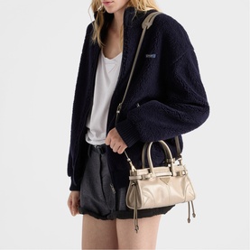 Model carrying Prada Accessories neutral mini bag with top handles and crossbody strap, styled with navy fleece jacket and black shorts.