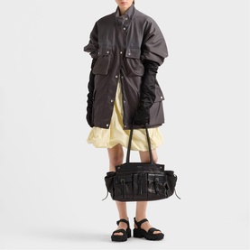 Model carrying black multi-pocket utility bag with ruched detailing, styled with dark oversized coat and yellow mini dress